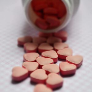 Close-up of heart-shaped pink pills spilled from a bottle on a soft surface.