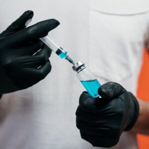 Gloved hands handling a syringe filled with blue liquid for medical use.